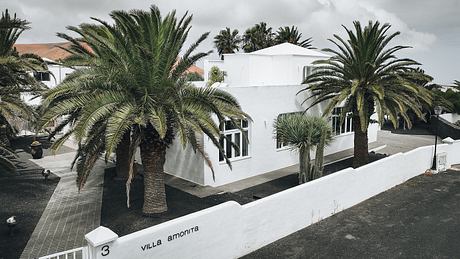 White, modern villa with palm trees and cloudy sky in the background.