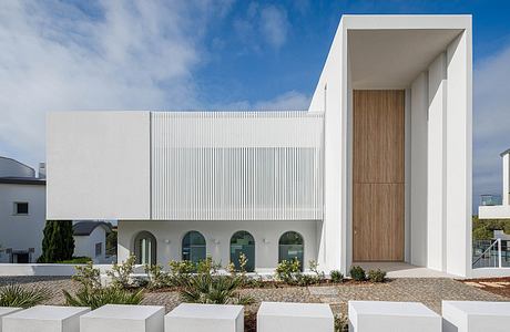 Modern architectural facade with geometric patterns, wooden entrance, and lush landscaping.