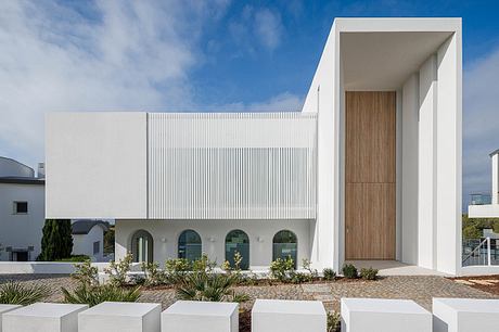 Modern architectural facade with geometric patterns, wooden entrance, and lush landscaping.