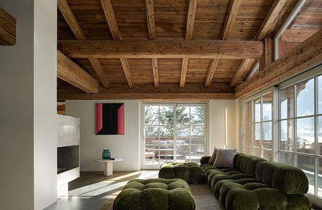 A cozy living space with a wooden ceiling, large windows, and green modular sofa.