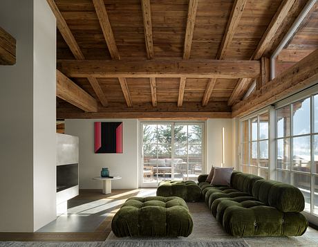 A cozy living space with a wooden ceiling, large windows, and green modular sofa.