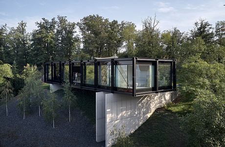 A modern, glass-walled structure nestled in a lush, wooded landscape.