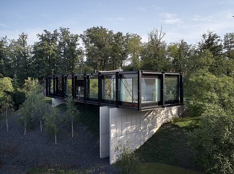 A modern, glass-walled structure nestled in a lush, wooded landscape.