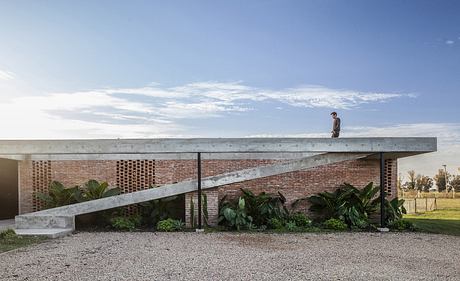 A modernist architectural structure with a raised concrete deck, brick walls, and lush greenery.