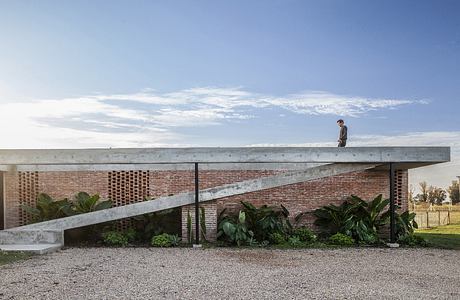 A modernist architectural structure with a raised concrete deck, brick walls, and lush greenery.