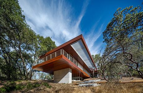 Modern, elevated home with wooden accents, surrounded by lush trees and open landscape.