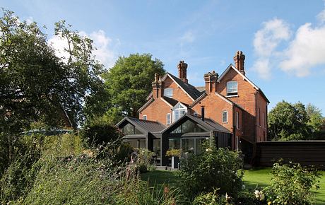 An impressive brick house with large windows, chimneys, and surrounding greenery.