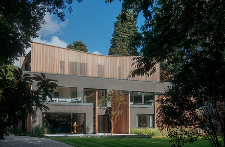 A modern, wood-clad building with large glass windows nestled in a lush, green landscape.