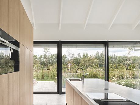 Spacious open-plan kitchen with floor-to-ceiling glass doors overlooking lush garden.