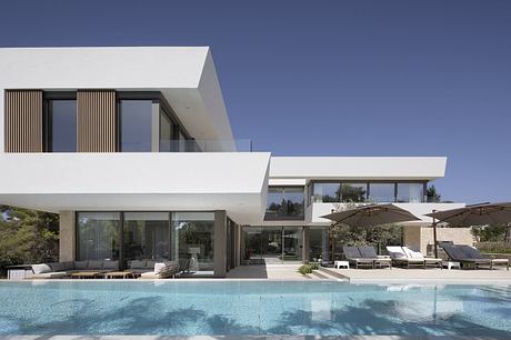 Modern minimalist villa with sleek architectural features, large glass panels, and an inviting poolside terrace.
