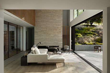 Spacious modern living room with wooden accents, large windows, and a view of the outdoor landscaping.