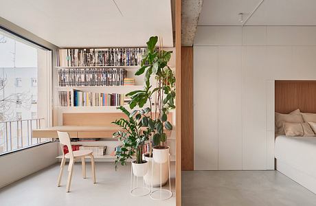 Modern apartment interior featuring built-in bookshelves, minimalist furnishings, and lush plants.