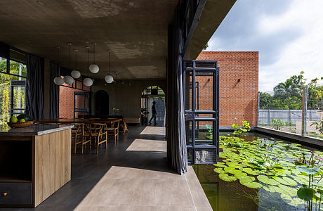 A modern open-concept kitchen and dining area overlooking a tranquil pond surrounded by lush greenery.