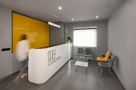 Modern reception area with clean lines, gray chairs, and a large yellow accent wall.