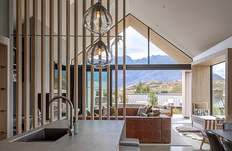 A modern kitchen with a concrete countertop, wooden beams, and large windows showcasing a scenic view.