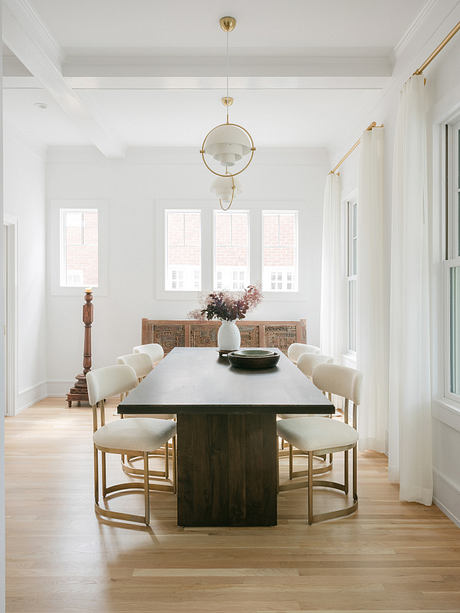 A bright, airy dining room with tall windows, a large wooden table, and elegant chairs.