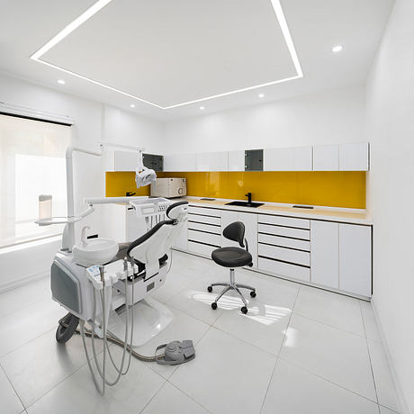 A modern, minimalist dental office with sleek white cabinetry, bright yellow backsplash, and sophisticated lighting.