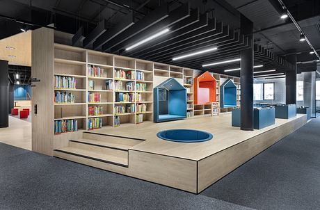 Spacious library with modular wooden shelves, colorful seating, and recessed ceiling lighting.