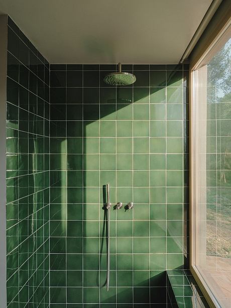 A modern, green-tiled bathroom with a large overhead shower and glass window.