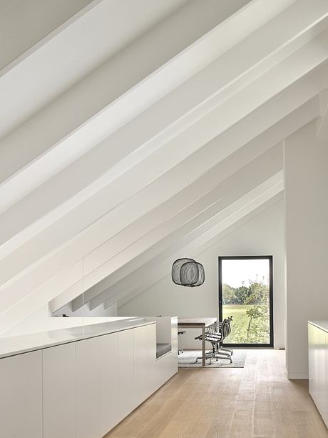 Modern interior with sleek white cabinetry, angled ceiling beams, and large window offering scenic views.