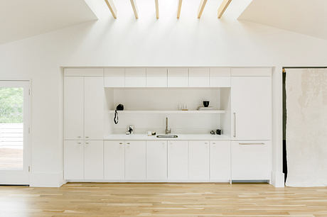 A minimalist, modern kitchen with sleek white cabinetry and warm wood flooring against a bright, airy space.