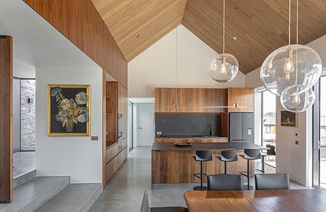 Modern open-plan kitchen and dining area with wooden walls, suspended lighting, and artwork.