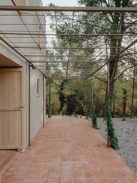 A covered walkway with a metal frame and tile floor leading to a wooden cabin in a forested area.
