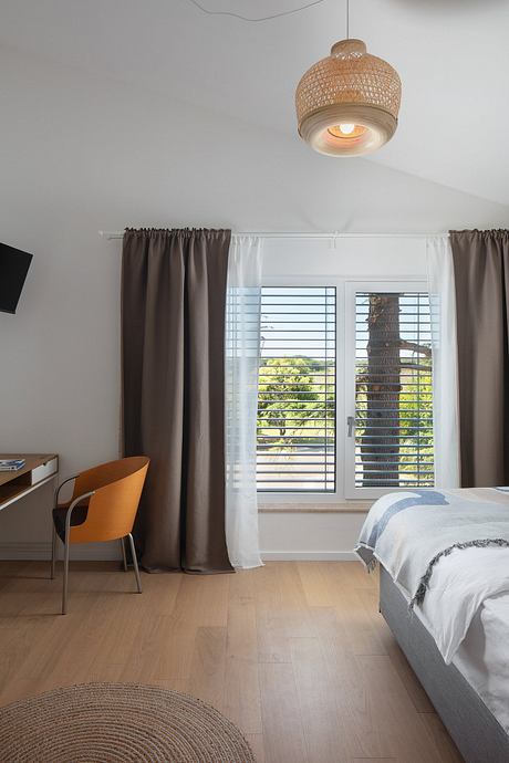 Cozy modern bedroom with woven pendant light, wooden floor, and large window overlooking nature.