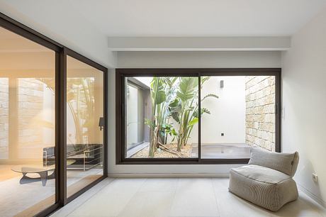 Minimalist living room with large glass windows overlooking lush outdoor vegetation.
