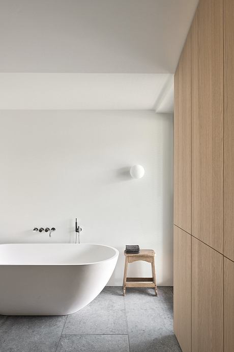 A modern bathroom with a white tub, wooden vanity, and sleek tile flooring.