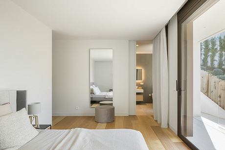 Spacious and minimalist bedroom with en-suite bathroom, floor-to-ceiling windows, and hardwood floors.