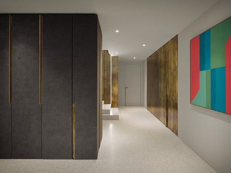 A modern, minimalist hallway with black and gold cabinets, colorful artwork, and terrazzo flooring.
