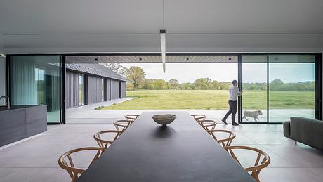 Minimalist modern interior with expansive glass walls overlooking a grassy field.