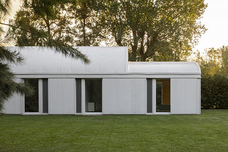 A modern, minimalist building with large windows set against a lush, green landscape.