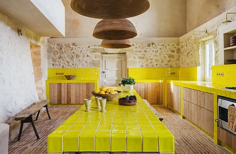 A vibrant yellow-tiled kitchen with rustic stone walls and unique wooden light fixtures.