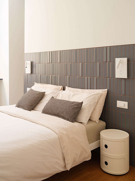 Minimalist bedroom design with gray tile backsplash, neutral bedding, and modern nightstand.