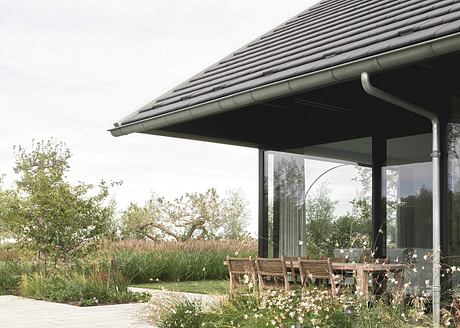 A covered patio with a slanted tile roof, surrounded by lush greenery and flowering plants.