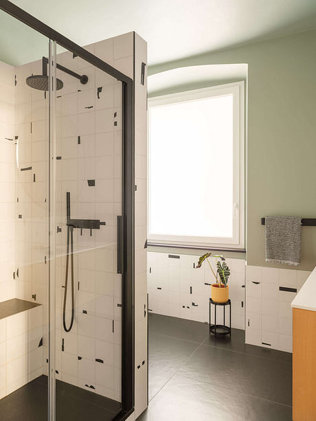 Well-designed modern bathroom with sleek glass shower enclosure, tiled walls, and potted plant.