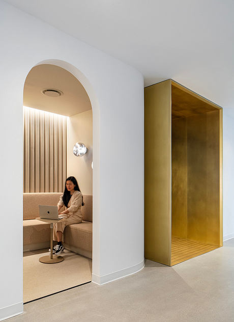 A modern interior with an arched niche, a laptop-equipped seating area, and a striking golden cabinet.