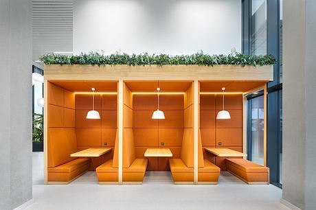 Modular seating areas in warm orange hues, with overhead planting creating a natural division.