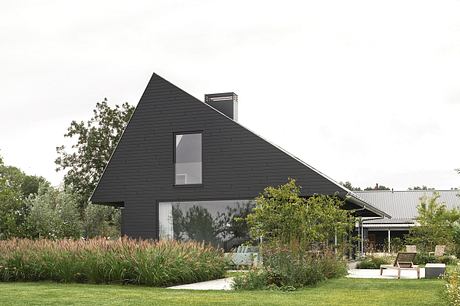 A modern, dark-clad structure with a prominent roofline, surrounded by lush greenery.