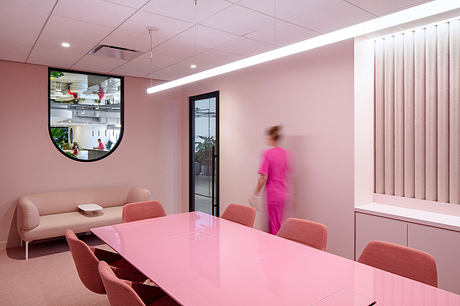 A modern, bright pink room with a large glass window, minimalistic furniture, and a person in motion.