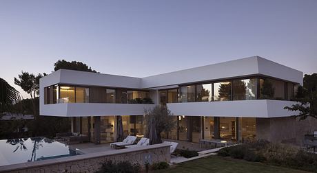 Contemporary two-story home with sleek, angular architecture and large glass windows overlooking a pool.