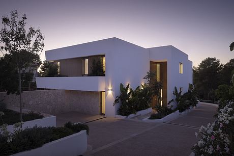 A modern, minimalist house with clean lines, warm lighting, and lush landscaping.