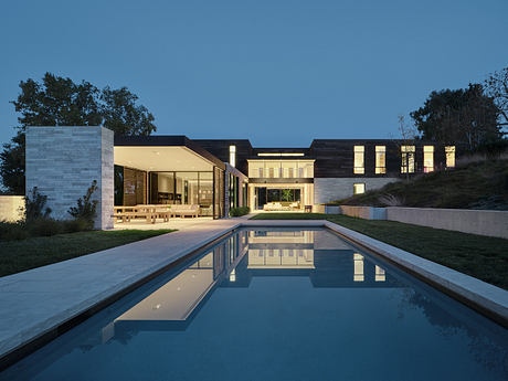 A modern two-story house with a sleek design, large windows, and a reflective pool.