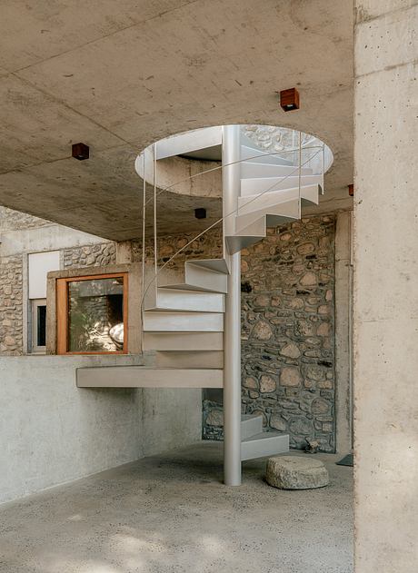 A spiral staircase in an interior space with concrete walls and a stone window frame.