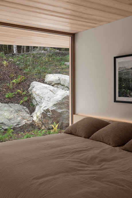 Cozy bedroom with wood-paneled ceiling and large window overlooking natural landscape.