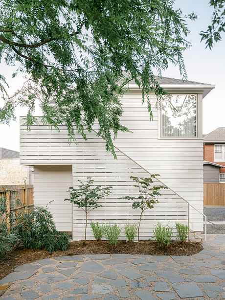 Modern, minimalist exterior with slatted wood siding, flagstone patio, and lush foliage.