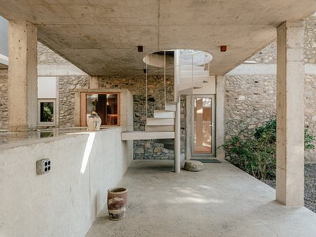 Concrete and stone interior with spiral staircase and natural lighting.