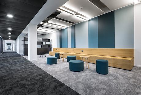 A modern office space with sleek wooden furniture, padded stools, and minimalist lighting.